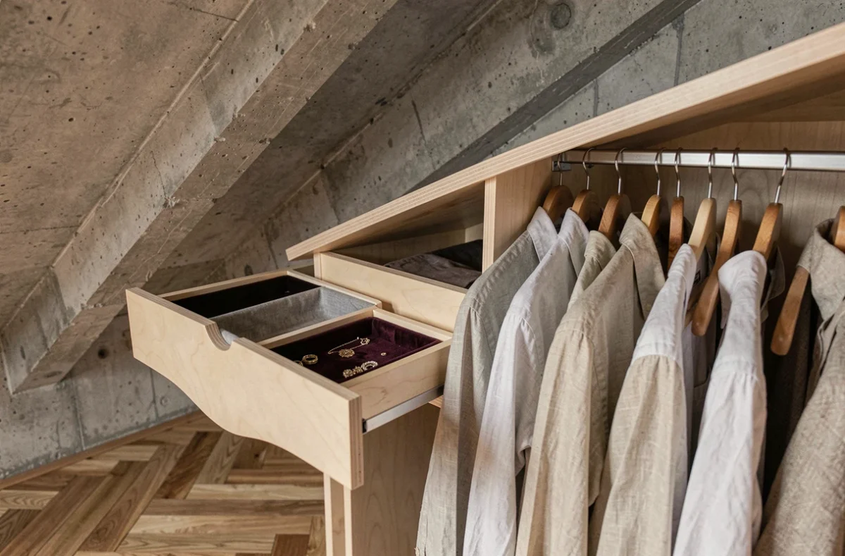 Détail d'un tiroir et d'une penderie dans un meuble de dressing intégré sous les combles avec revêtement en velours